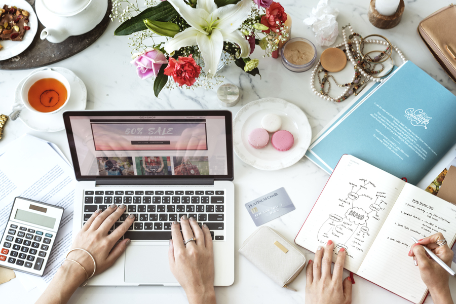 Two pairs of hands of Businesswomen calculating Esty fees on a laptop and notebook.