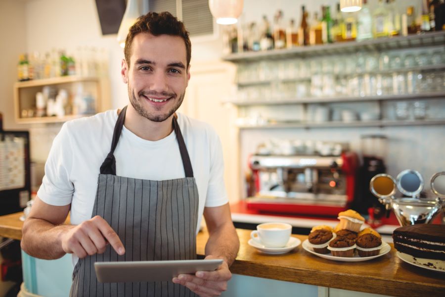 A barista in a cafe working on a tablet in front of the cafe's bar. 