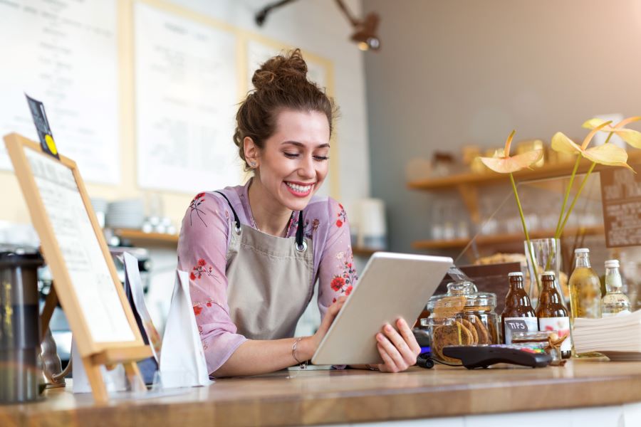 The cafe's owner works on a tablet to Boost her Cafe's Business with Online Tools.