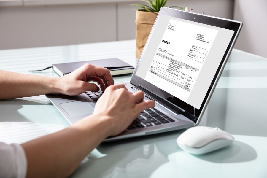 A Businesswoman's Hand Checking Invoice On Laptop 
