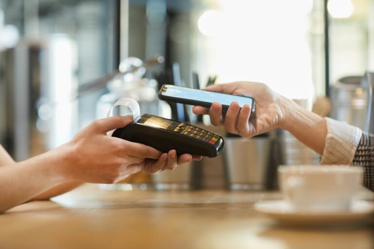 A customer's hand holding a smartphone with the Google Wallet and paying on a card terminal.